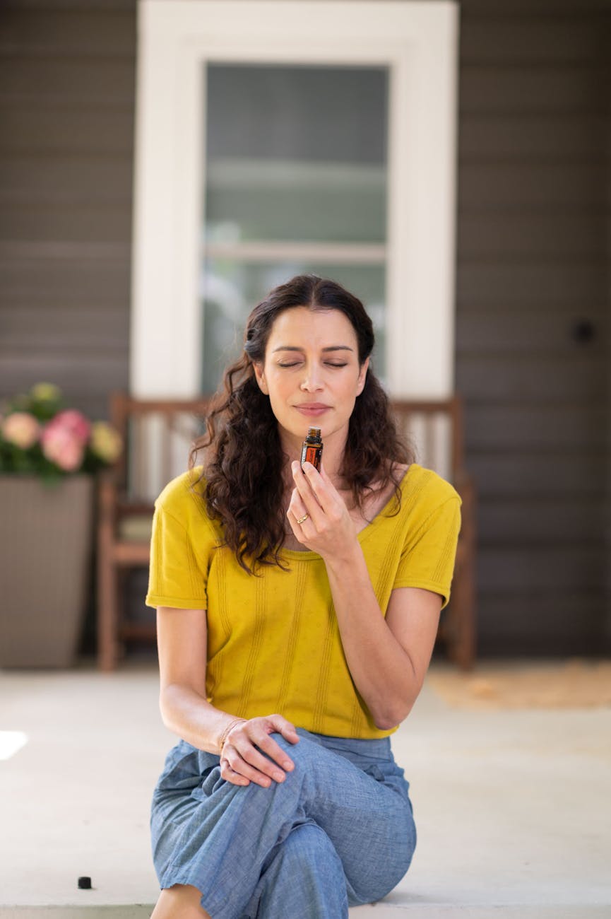 woman in yellow crew neck t shirt holding and smelling an essential oil