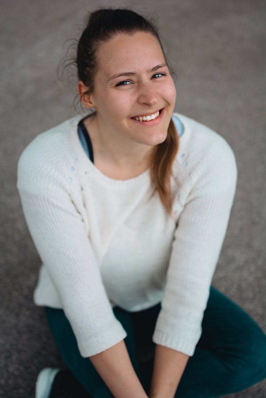 a woman sitting on the asphalt ground while smiling at the camera