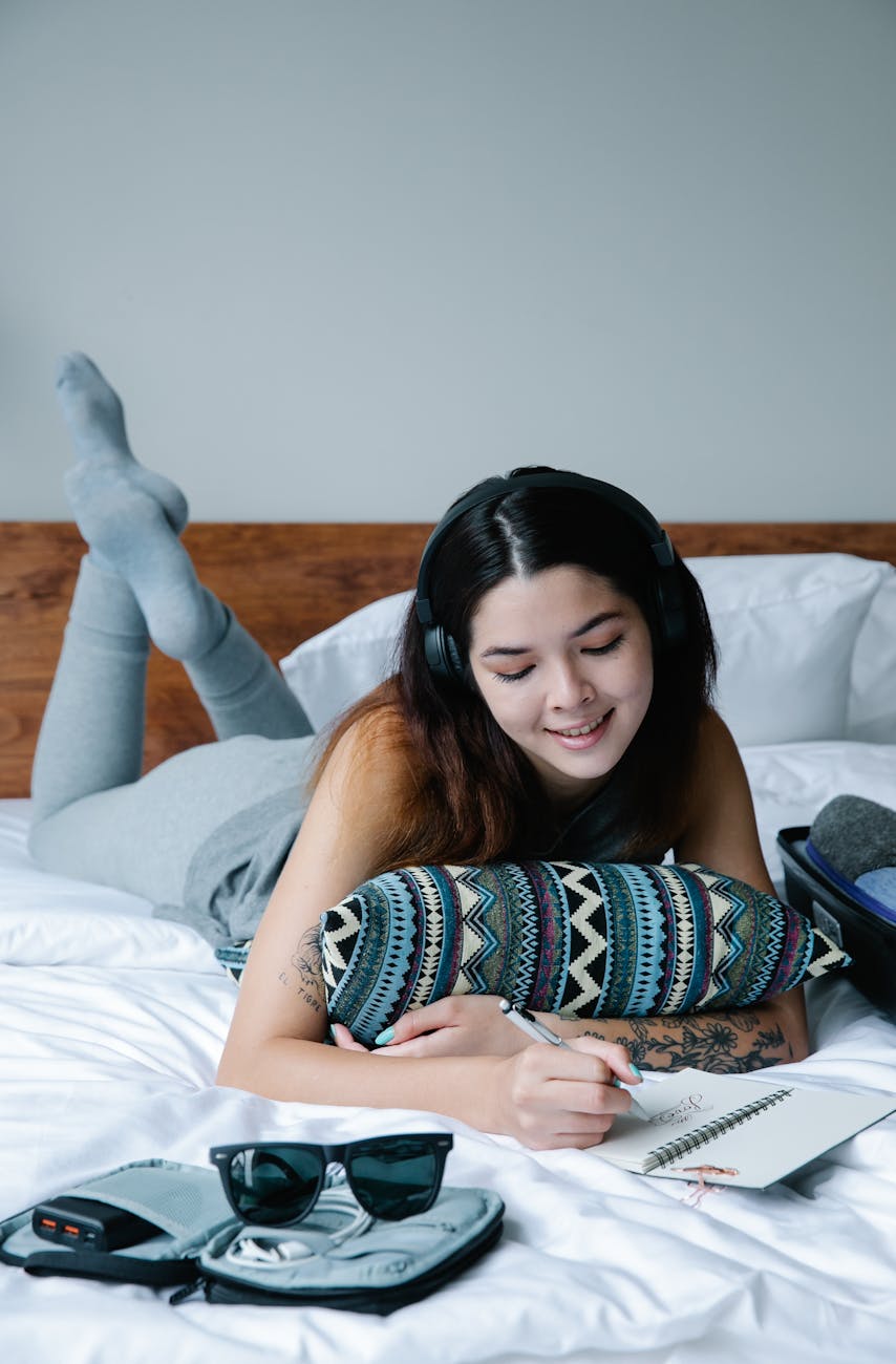 a woman lying on front in bed writing on a notebook